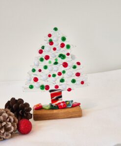 Glass Christmas tree with red, green, and white decorations on a wooden base, surrounded by pinecones and a red ornament.