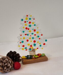 Glass Christmas tree with colorful dots, surrounded by pinecones and a red glittery ornament on a white surface.