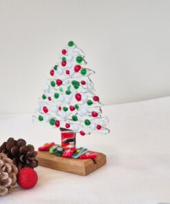 Glass Christmas tree with red, green, and white beads on a wooden base, surrounded by pinecones and a red glitter ball.