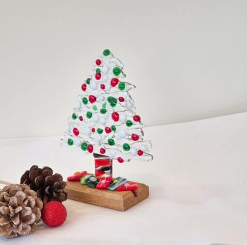 Glass Christmas tree with red, green, and white beads on a wooden base, surrounded by pinecones and a red glitter ball.