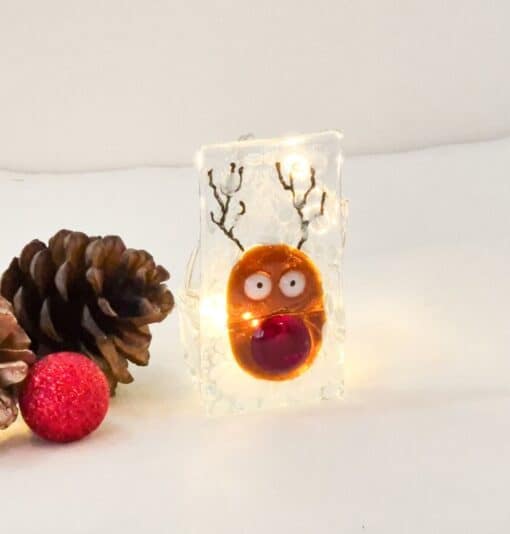 Festive reindeer decoration with lights alongside pinecones and a red ornament on a white background.