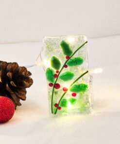 Decorative glass with holly design, surrounded by pinecones and lights on a white background.