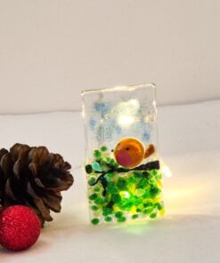 Glass ornament with a small bird and green beads, lit from inside. Two pinecones and a red ornament sit beside it.