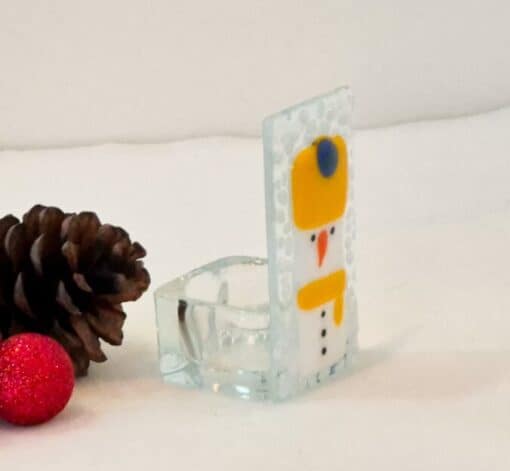 Glass snowman decoration with pinecones and a red glitter bauble on a white surface.