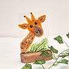 Glass artwork of a giraffe with green leaves, mounted on a wooden base, against a neutral background.