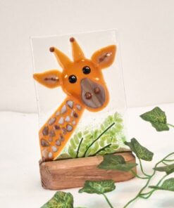 Glass artwork of a giraffe with green leaves, mounted on a wooden base, against a neutral background.