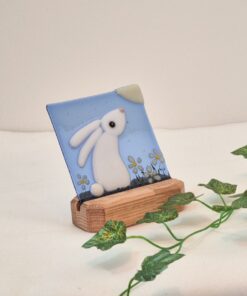 Glass art featuring a white rabbit with flowers on a blue background in a wooden stand, decorated with a green vine.