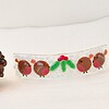 Glass ornament with red and green details next to two pine cones and a glittery red ball on a white surface.