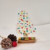 Glass Christmas tree with colorful dots, pinecones, and a red ornament on a white surface.