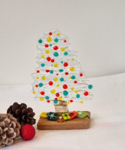 Glass Christmas tree with colorful dots, pinecones, and a red ornament on a white surface.