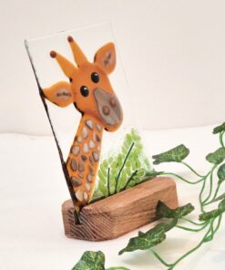 Glass artwork of a giraffe with a wooden base and green leaves, set against a light background.