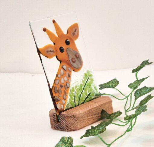 Glass artwork of a giraffe with a wooden base and green leaves, set against a light background.