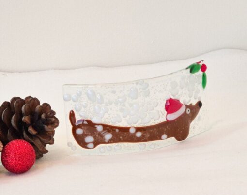 Festive glass ornament with a reindeer, Santa hat, pine cones, and a red bauble on a white background.