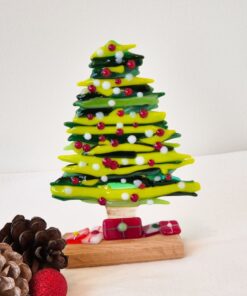 Glass Christmas tree with red and white ornaments, pinecones, and a red bauble on a white surface.