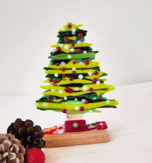 Glass Christmas tree with red and white ornaments, pinecones, and a red bauble on a white surface.