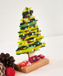 Glass Christmas tree with colorful ornaments on a wooden base, surrounded by pinecones and a red glittery ball.