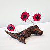 Three vivid red glass flowers on a textured brown driftwood base against a plain background.