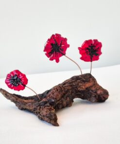 Three vivid red glass flowers on a textured brown driftwood base against a plain background.