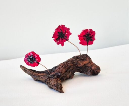 Three vivid red glass flowers on a textured brown driftwood base against a plain background.