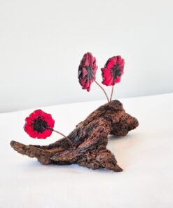 Three red glass poppies on a textured wooden base, set against a plain white background.