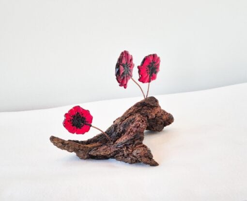 Three red glass poppies on a textured wooden base, set against a plain white background.