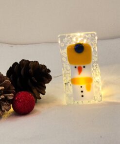 Glass snowman ornament with string lights, pine cones, and a red glitter ball on a white surface.