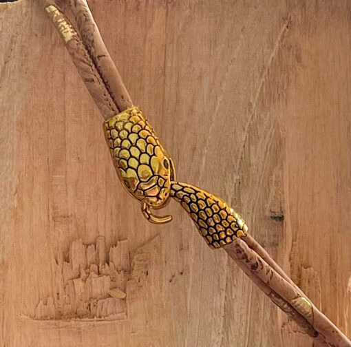 Gold snake-shaped clasp on a beige cork bracelet against a wooden background.