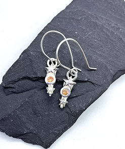 Silver star-themed earrings with orange gemstones displayed on a dark slate background.