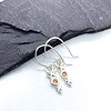 Silver earrings with orange gemstone stars, placed on a dark slate surface.