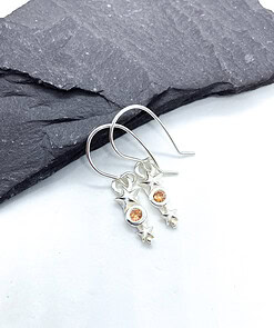 Silver earrings with orange gemstone stars, placed on a dark slate surface.