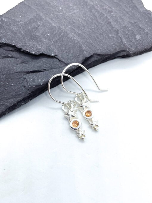 Silver earrings with orange gemstone stars, placed on a dark slate surface.