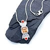 Silver necklace featuring a pendant with an orange square gemstone and two red round gems, displayed on dark stone.