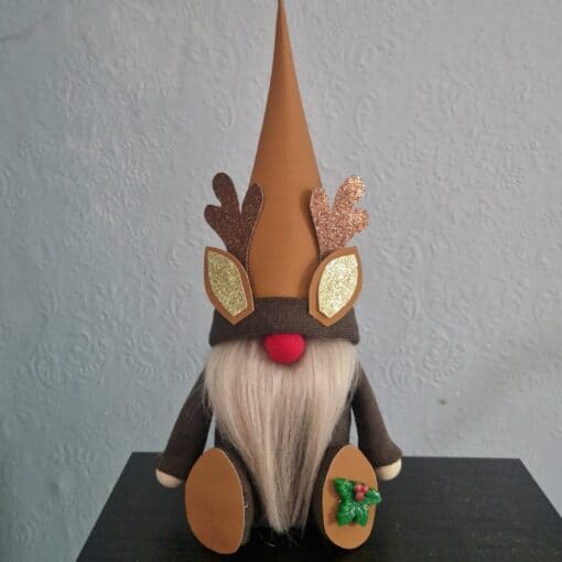 Gnome with a reindeer hat, long white beard, and holly decoration, sitting against a textured blue background.