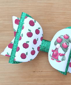 A colorful hair bow with an apple pattern and a gnome design on a wooden background. The bow has green glitter accents.