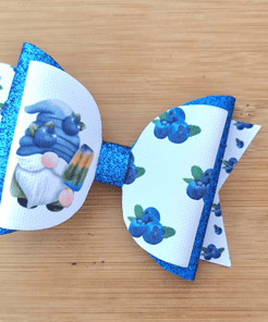 Blue and white bow featuring a gnome with blueberries, a glittery blue center, and a wooden background.