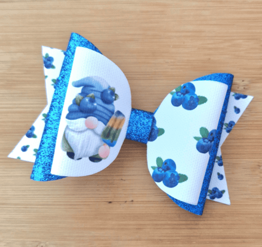 Blue and white bow featuring a gnome with blueberries, a glittery blue center, and a wooden background.