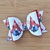 White hair bow with red trim featuring gnome designs holding pitchforks, placed on a wooden surface.