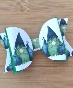 White hair bow with green and black gnome pattern, accented with green glitter edges, on a wooden background.