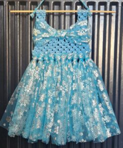 Blue and white crocheted dress with a snowflake pattern, hanging on a wooden rod against a black corrugated background.