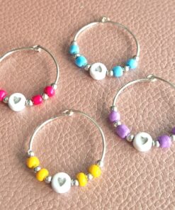 Colorful wine glass charms with beads in red, blue, purple, and yellow on a leather-textured surface.