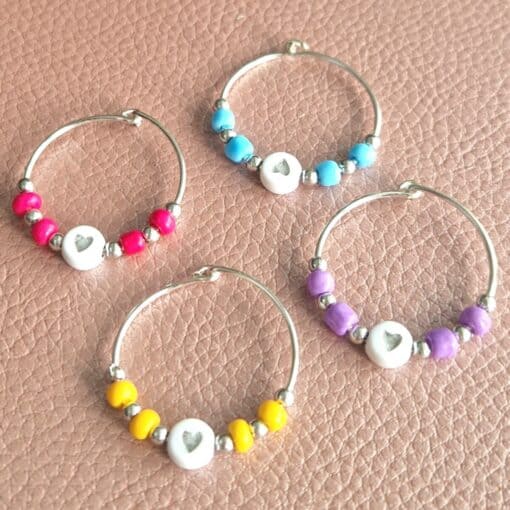 Colorful wine glass charms with beads in red, blue, purple, and yellow on a leather-textured surface.