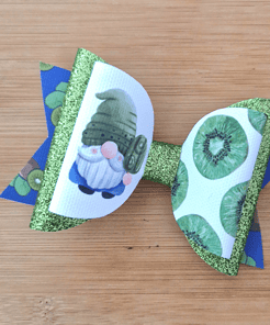 A decorative bow with glittery green loops and images of a gnome and sliced kiwis on a wooden surface.