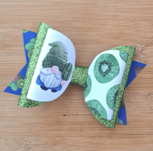 A decorative bow with glittery green loops and images of a gnome and sliced kiwis on a wooden surface.