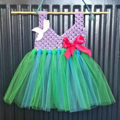 Handmade fairy dress with a purple crochet bodice, green tulle skirt, red bow, and white bird decoration, hanging on a rod.