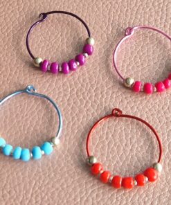 Four colorful beaded wine glass markers on a textured surface, featuring purple, pink, blue, and red wire rings with matching beads.