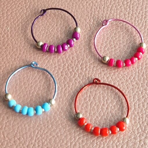 Four colorful beaded wine glass markers on a textured surface, featuring purple, pink, blue, and red wire rings with matching beads.