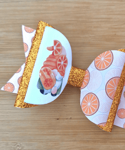 Orange-themed bow with glittery gold accents, featuring imagery of oranges and a gnome on a wooden surface.