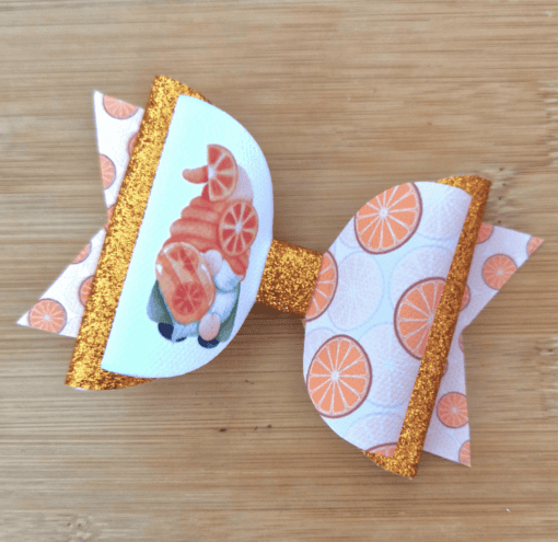 Orange-themed bow with glittery gold accents, featuring imagery of oranges and a gnome on a wooden surface.