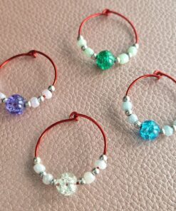 Four red wire wine glass charms with different colored beads: purple, green, blue, and clear, placed on a textured surface.