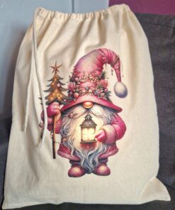 Cloth drawstring bag with a festive gnome holding a lantern and small decorated Christmas tree, sitting on a gray surface.